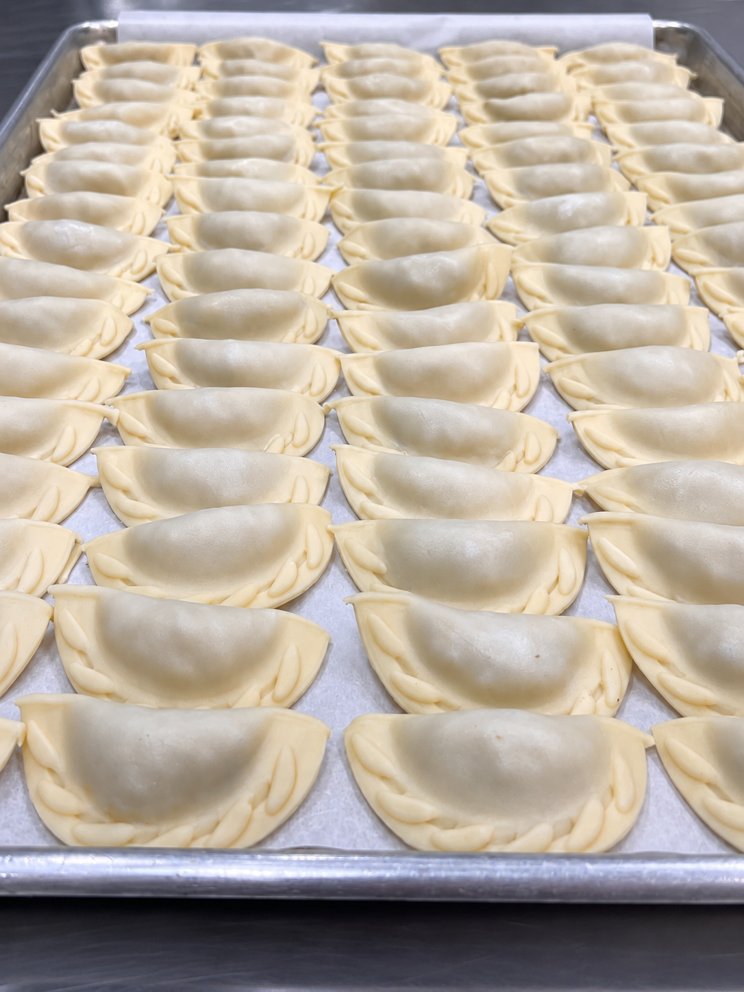Rows of uncooked Argentine empanadas arranged on a metal tray.