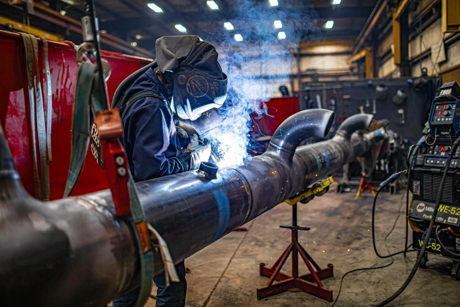 Welder performing pipe fabrication in an industrial workshop.