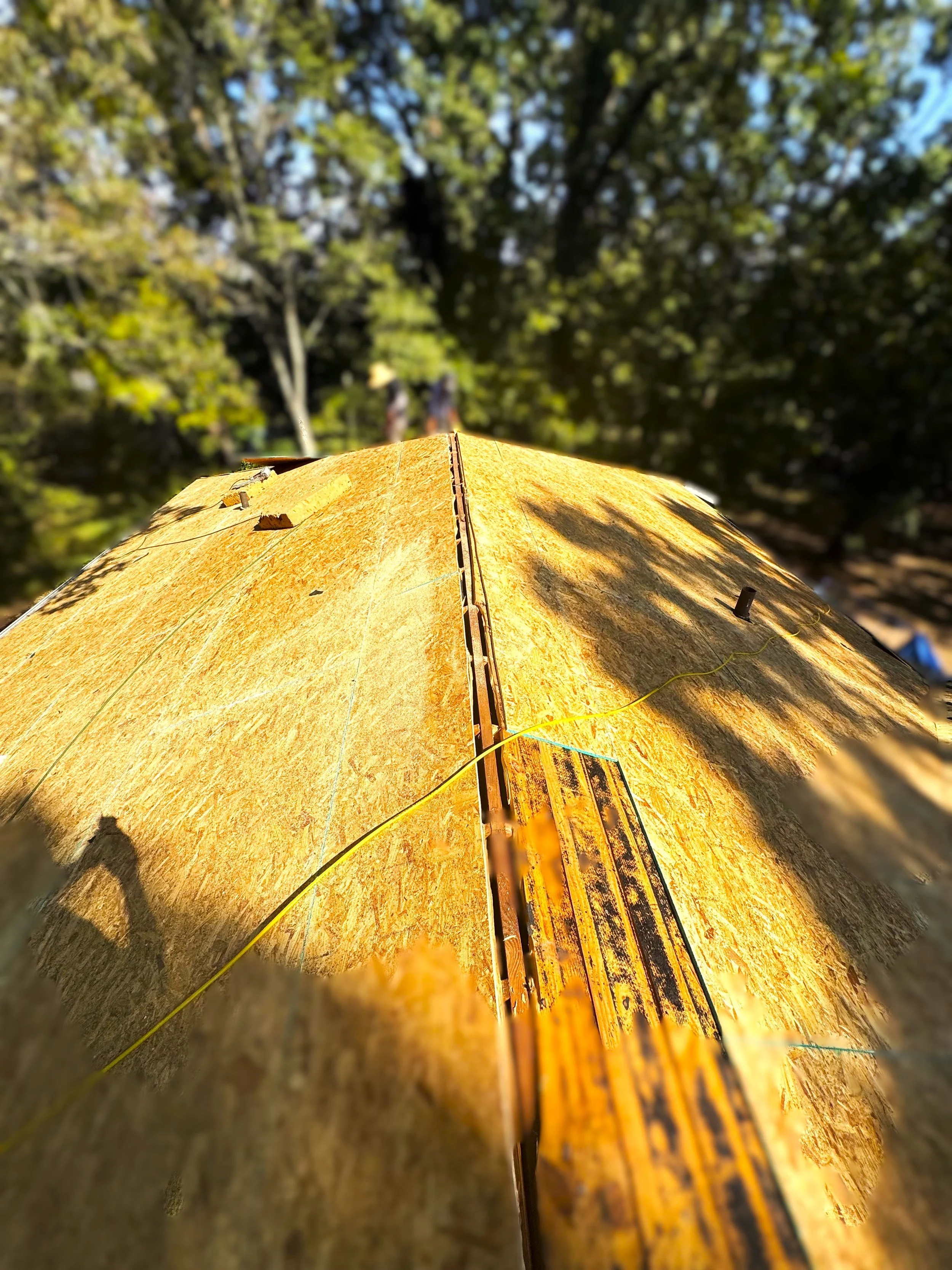 Close-up of a yellow wooden boat docked on water with trees and a blue sky reflected in the background.