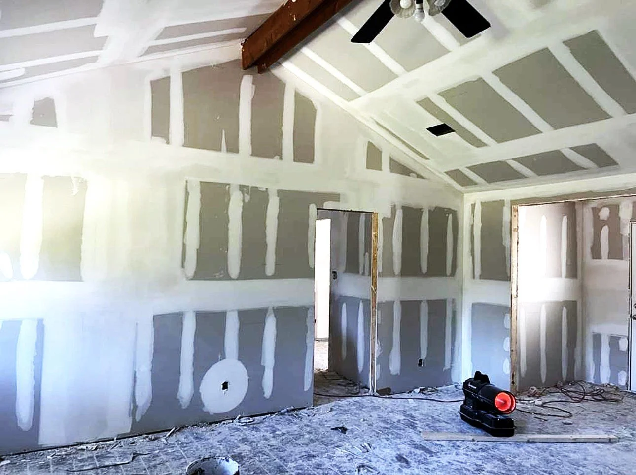 Interior of a house under construction with unfinished drywall, a ceiling fan, and construction tools on the floor.