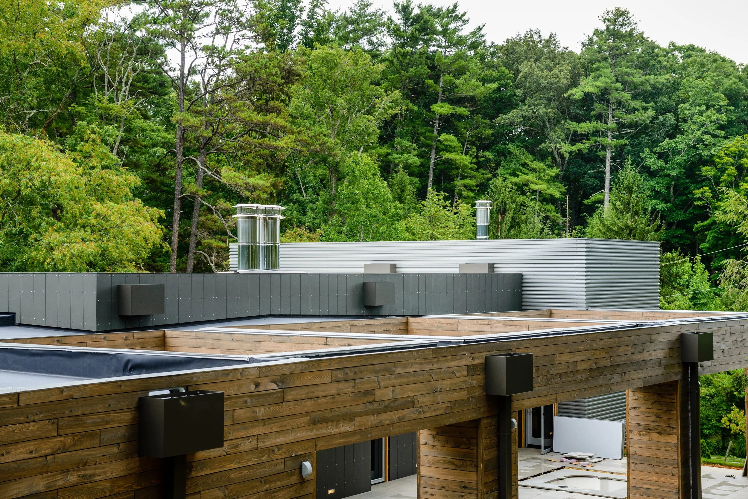 Modern building with wooden and metallic exterior, surrounded by green trees in the background.