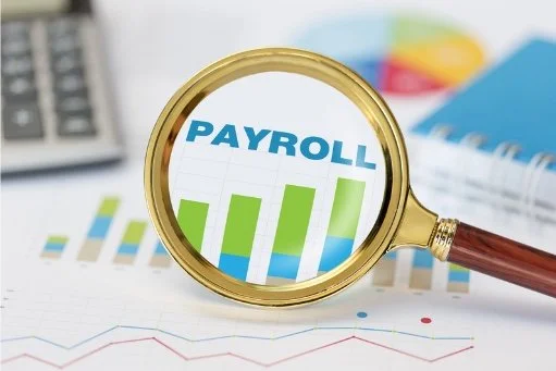 Magnifying glass examining payroll bar graph and financial charts on a desk.