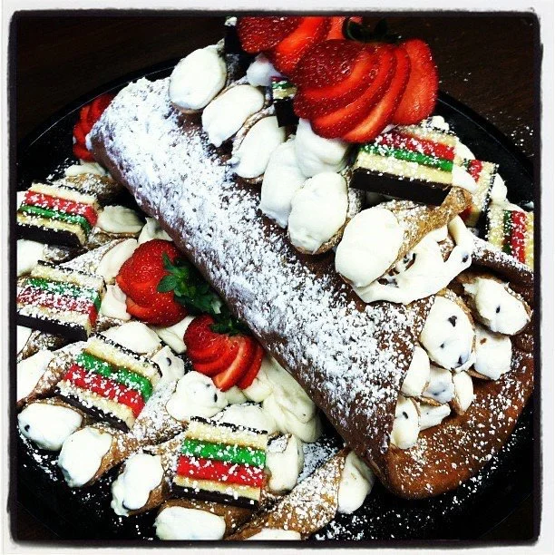 Christmas-themed dessert platter with cannoli, layered cake slices, strawberries, and whipped cream.
