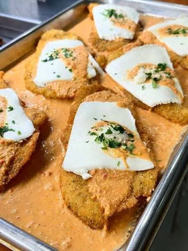 Fried fish fillets topped with slices of cooked squid and garnished with chopped herbs on a tray of seafood sauce.