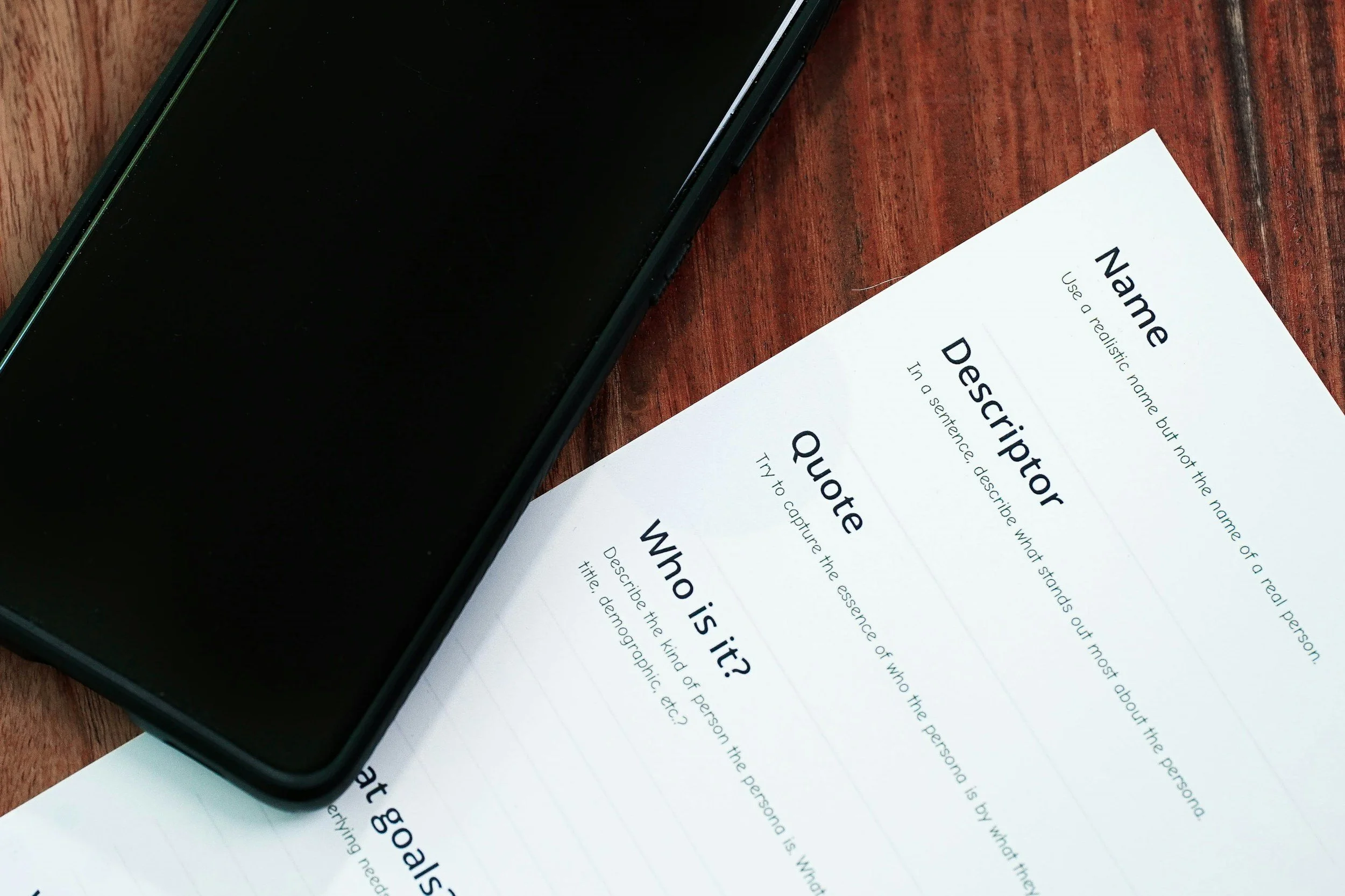 Close-up of a smartphone on a wooden surface next to a printed sheet with the question 'What is it?' and detailed instructions about describing the image for accessibility.