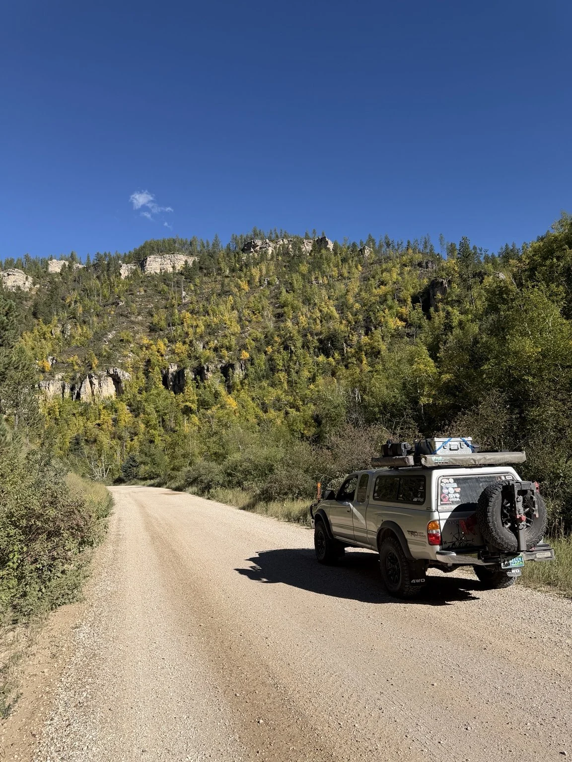 Randy’s Toyota Tacoma, Strider, equipped for overlanding on a forest road below rocky cliffs.