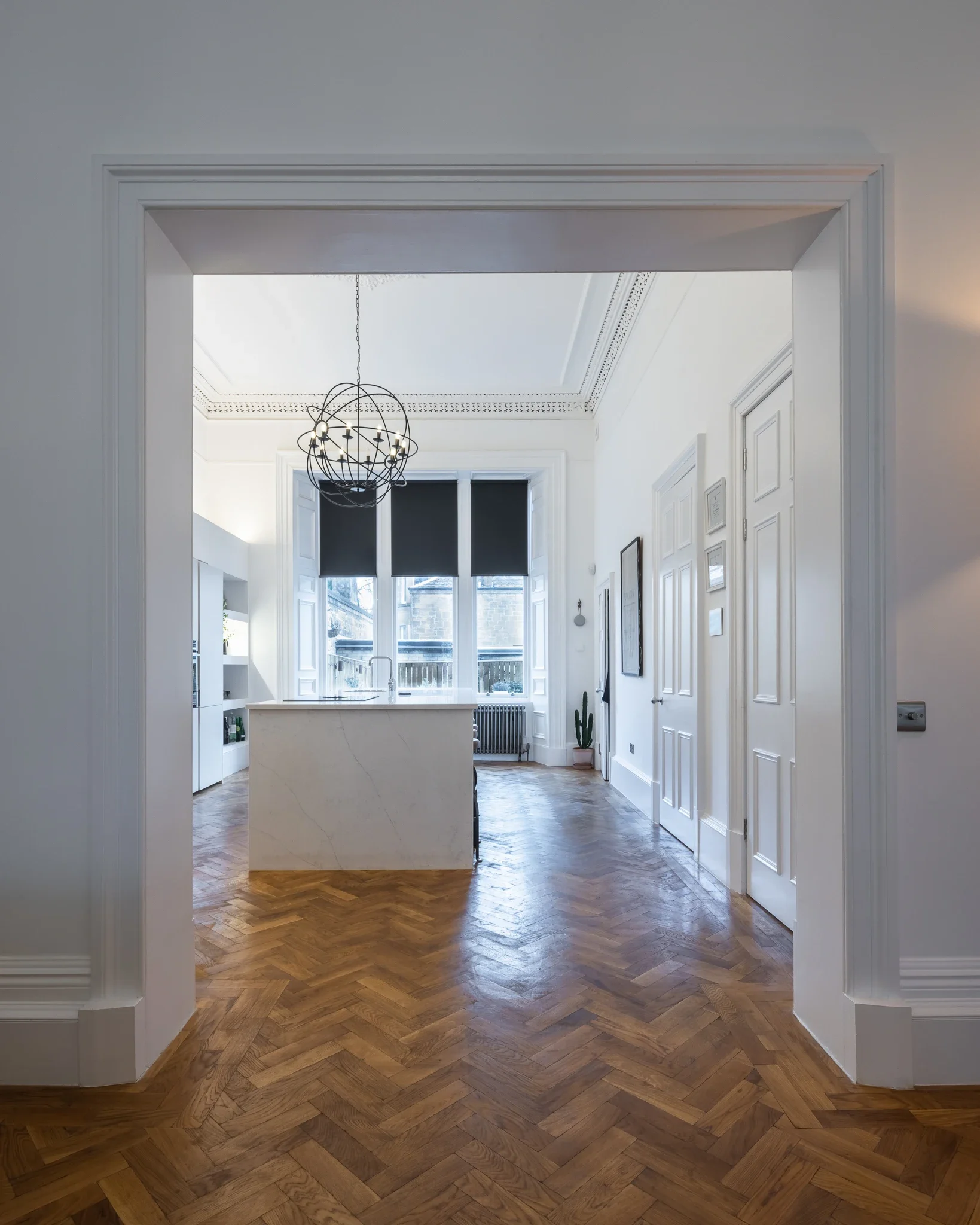 Bright modern kitchen with marble island, black globe pendant light, bay windows, white paneled doors, and herringbone wood flooring