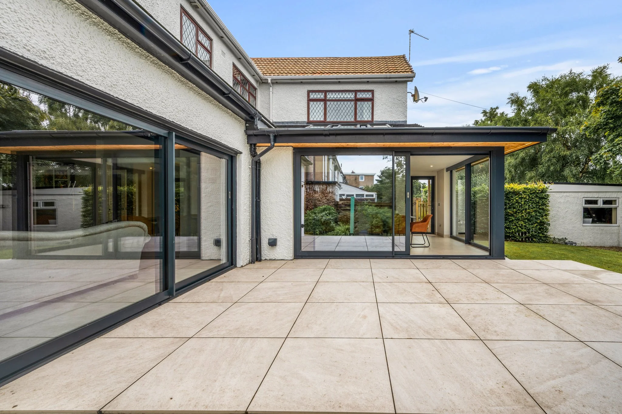 Modern glass-enclosed home extension opening onto a tiled patio and landscaped backyard