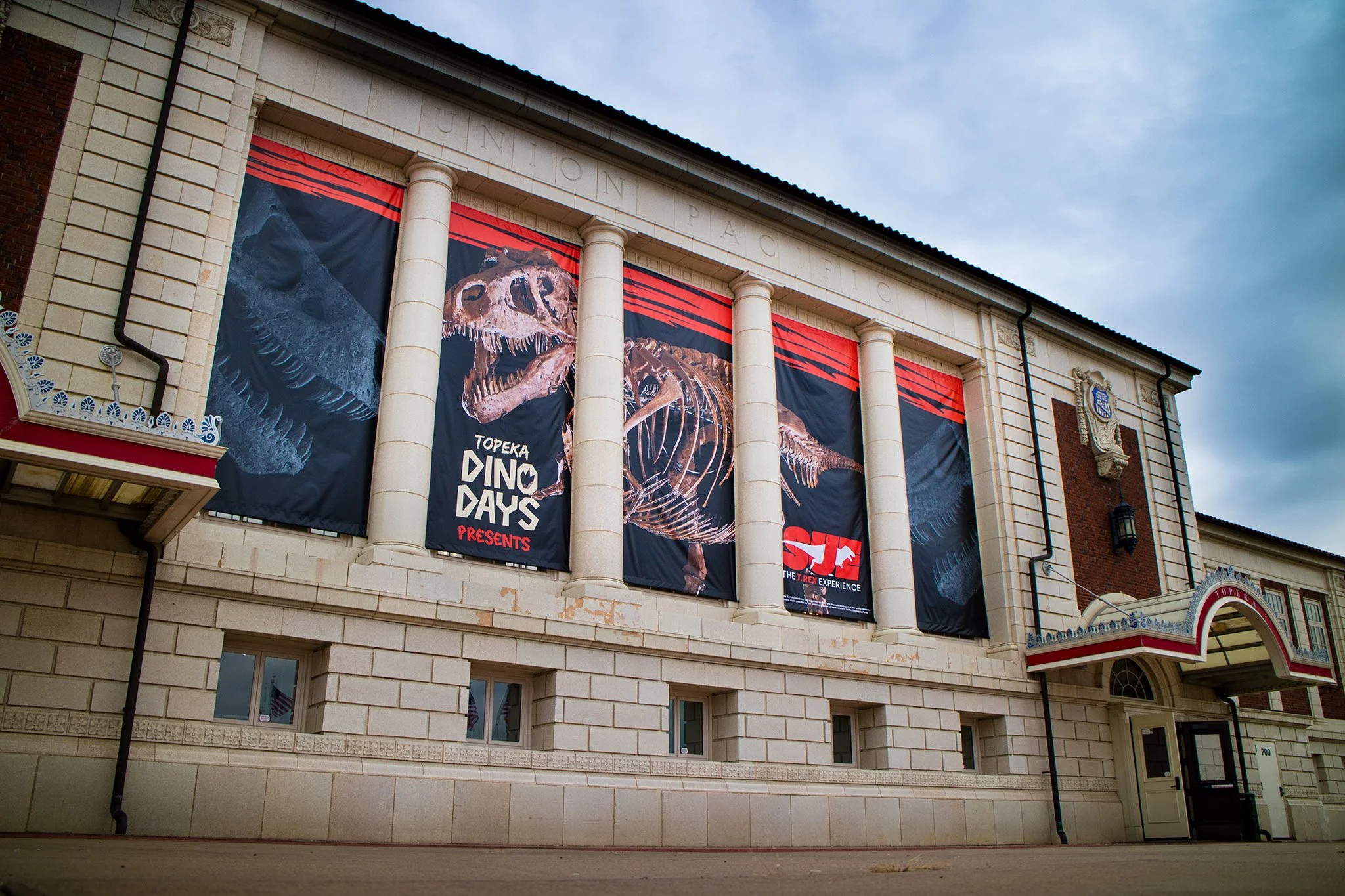 Exterior of a building with banners featuring dinosaur skeletons, advertising Topeka Dino Days.