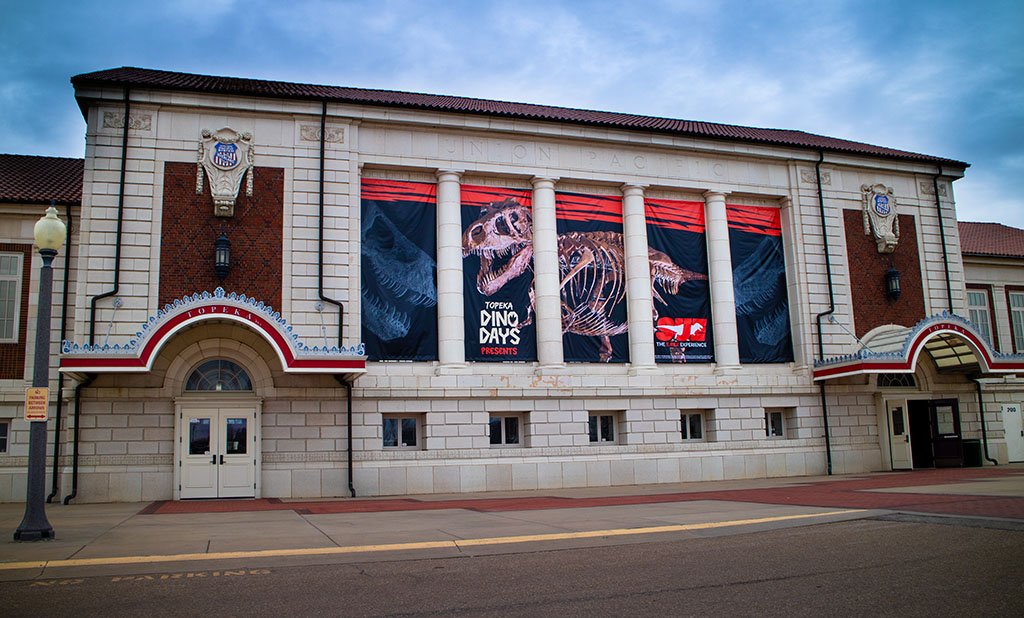 The exterior of a building with large banners displaying a dinosaur skeleton and the text "Topeka Dinosaur Days presents."