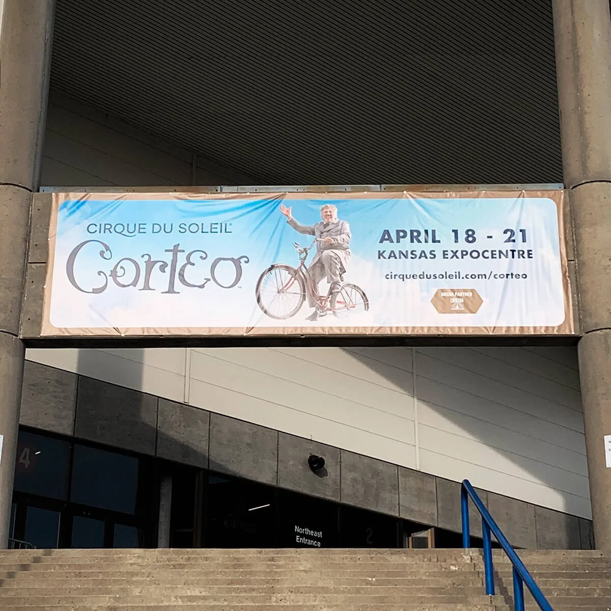 Banner advertising Cirque du Soleil's Corteo show at the Kansas Expocentre from April 18 to 21, featuring a man in a suit riding a bicycle and smiling.