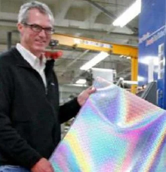 Man holding a holographic or reflective material in a warehouse or industrial setting.
