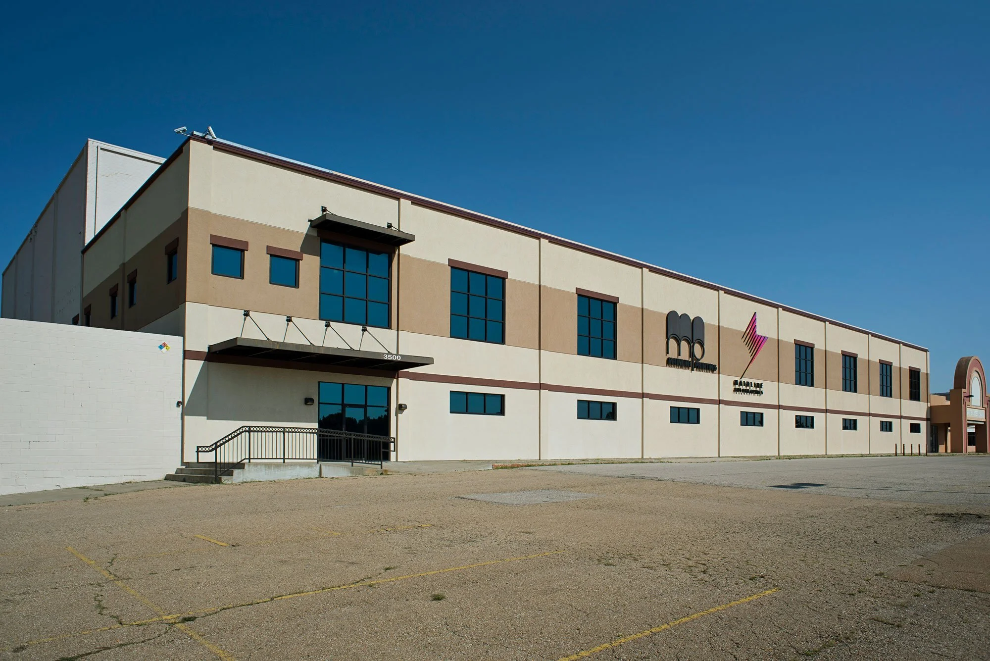 Empty parking lot in front of a large commercial building with company logos and a clear blue sky