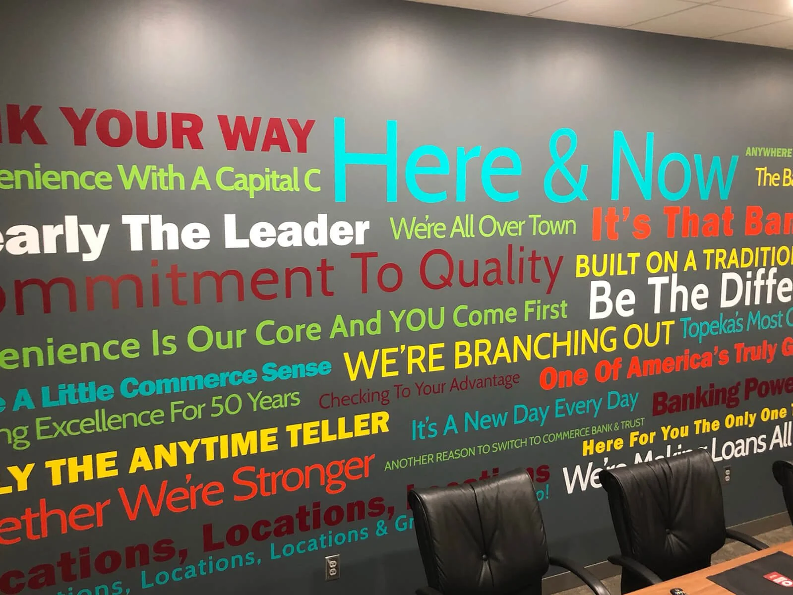 Wall with colorful motivational quotes about business and growth, with three black chairs and a table in front.