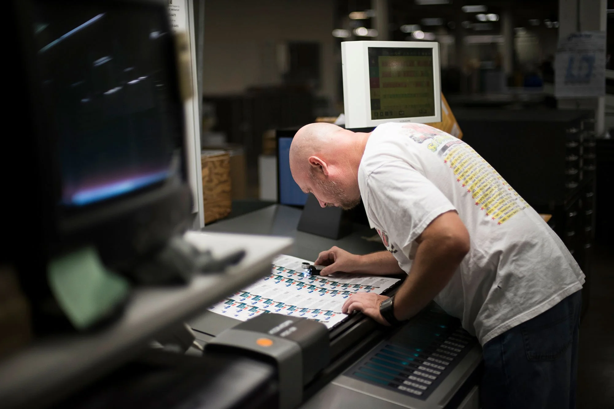 A man bending over a counter examines a sheet with stickers in a store or warehouse.