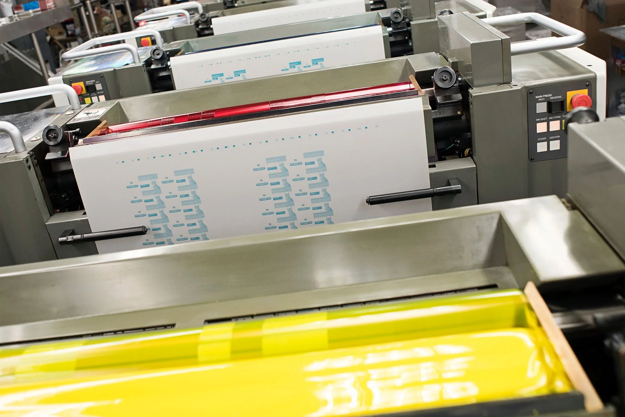 Industrial printing press with printed sheets of paper, surrounded by machinery and controls.