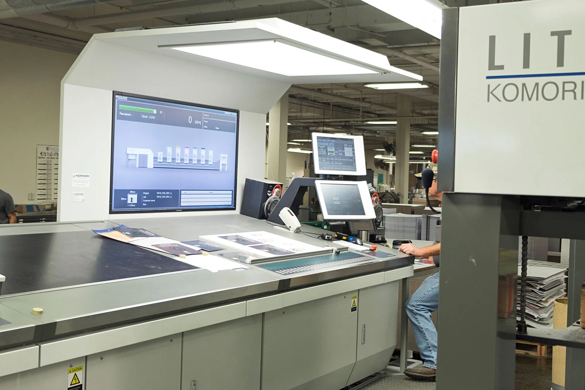 Industrial printing machine with computer screens and control panel in a factory setting.