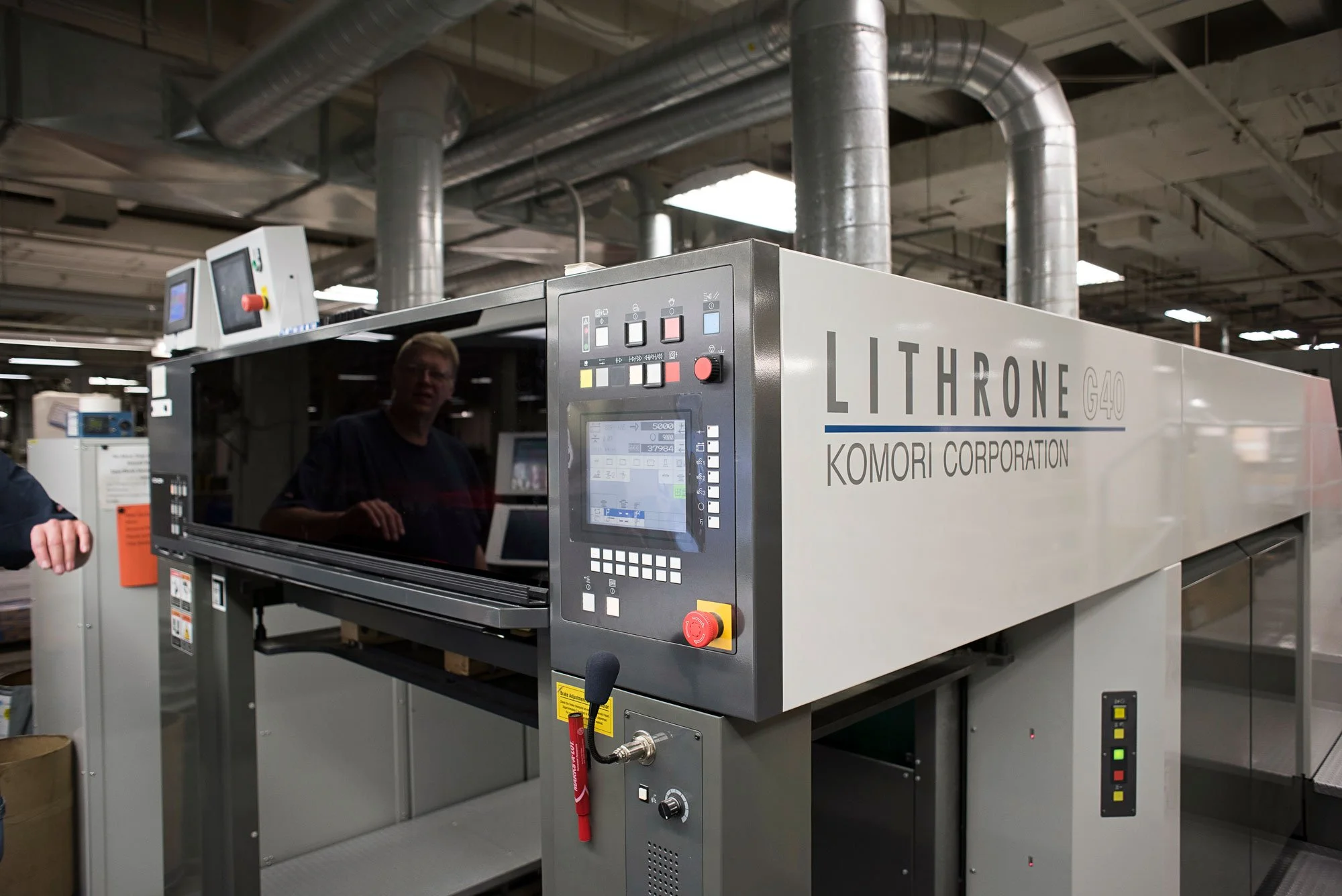 Industrial manufacturing equipment in a factory setting with control panels and ventilation ducts, labeled 'LITHRONE G40' by Komori Corporation.