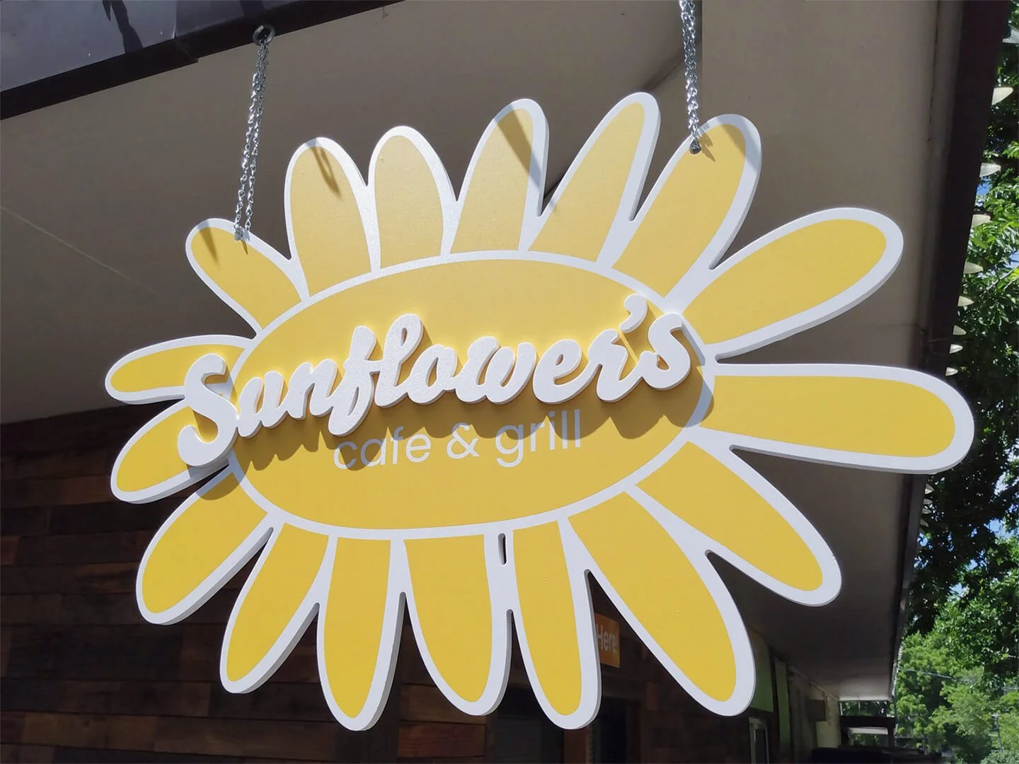 Hanging sign for Sunflowers cafe & grill with a yellow sunflower design and white cursive text