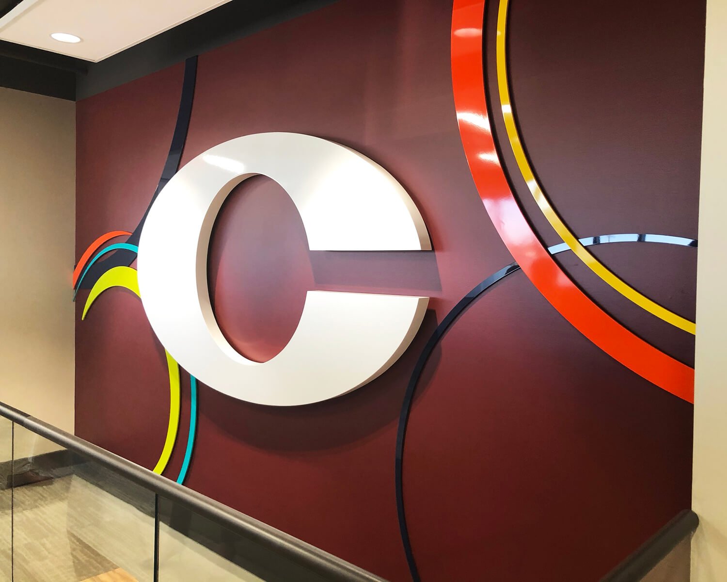 Wall art with a large white letter 'C' on a red background, surrounded by colorful curved lines in black, blue, yellow, and red.