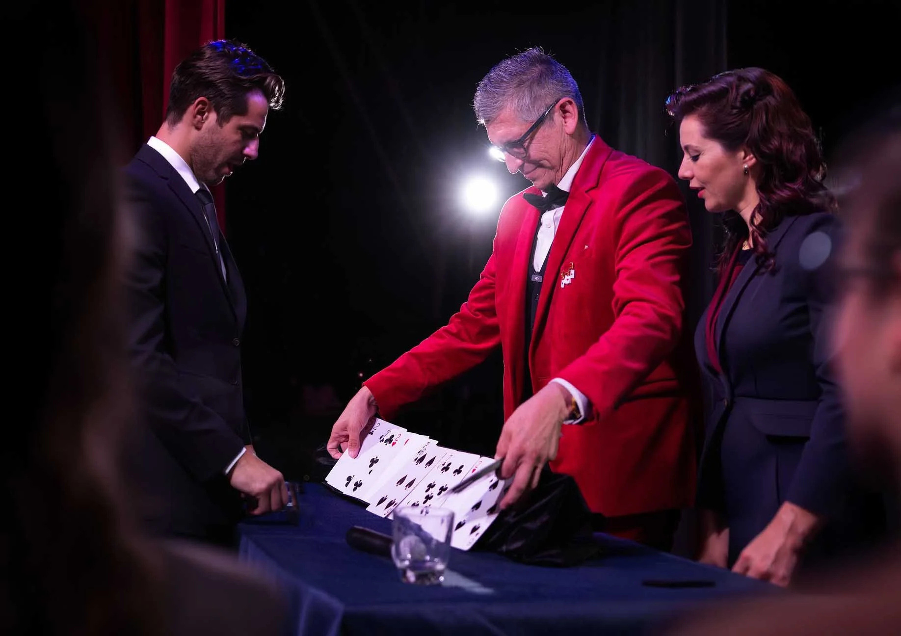 People playing and examining a deck of playing cards on stage during a performance or event, with dark background and bright stage lighting.