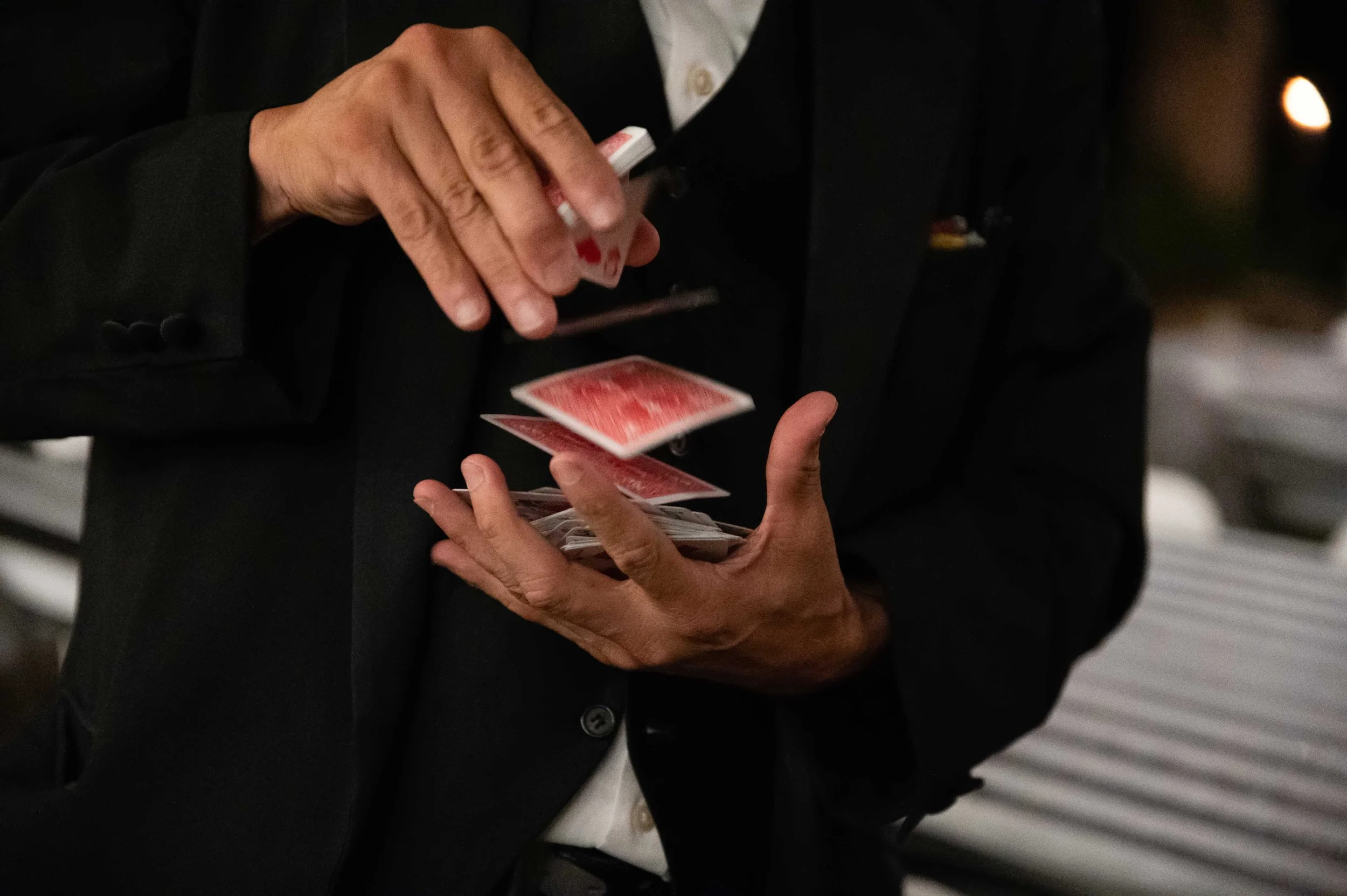 Close-up of a person in formal attire performing a card trick, holding playing cards with their hands, with a blurred background.