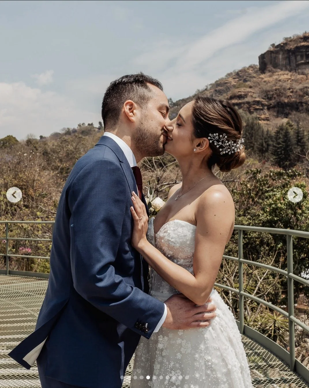 Bride with a low bun and pearl hair accessory, sharing a kiss outdoors