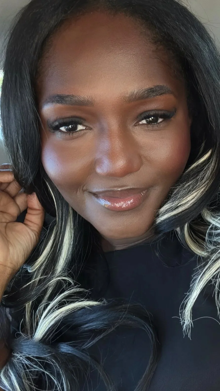 Close-up of a smiling African American woman with long black hair with blonde streaks, wearing makeup and a black top.