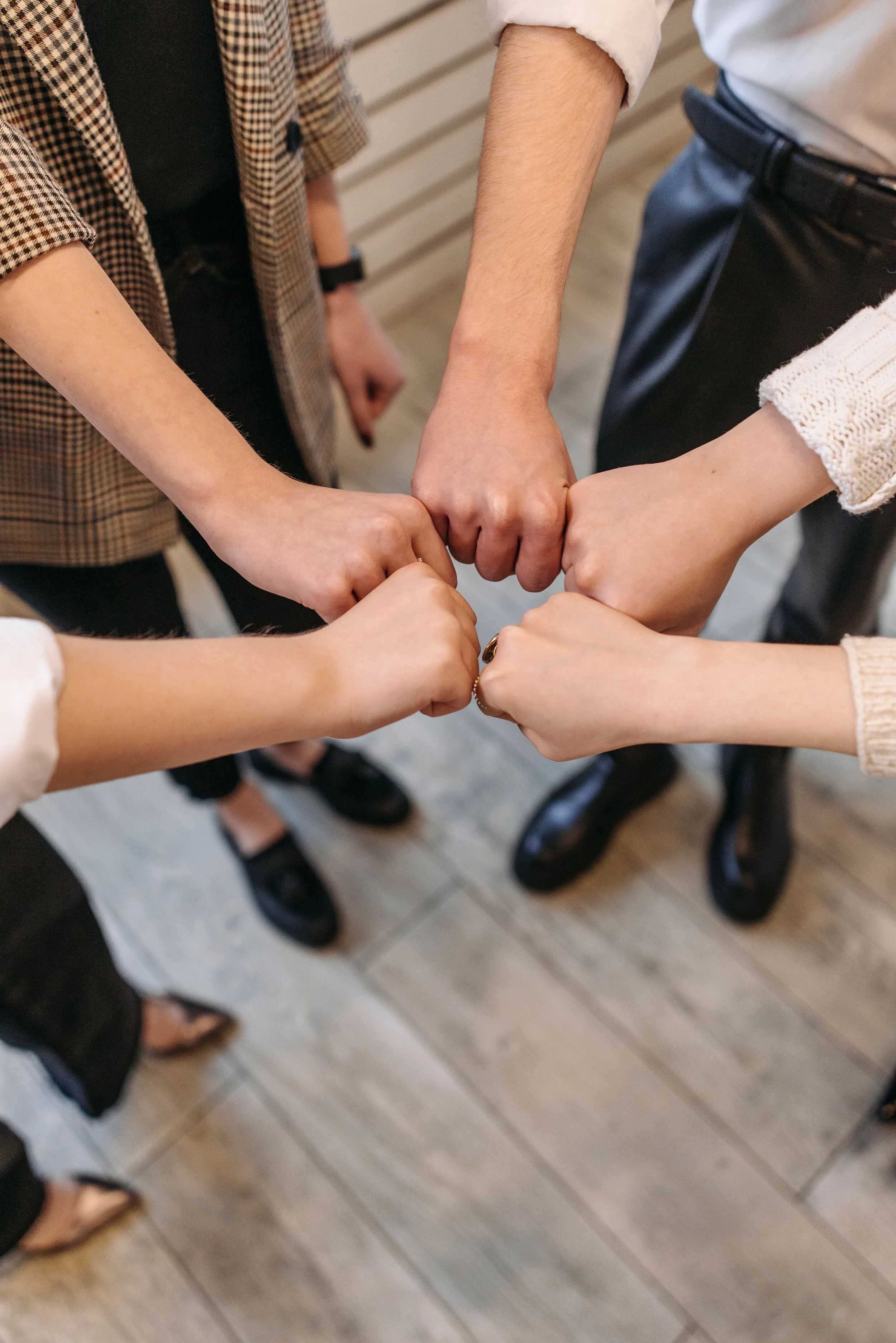 Four people standing in a circle with their fists joined together in the center.