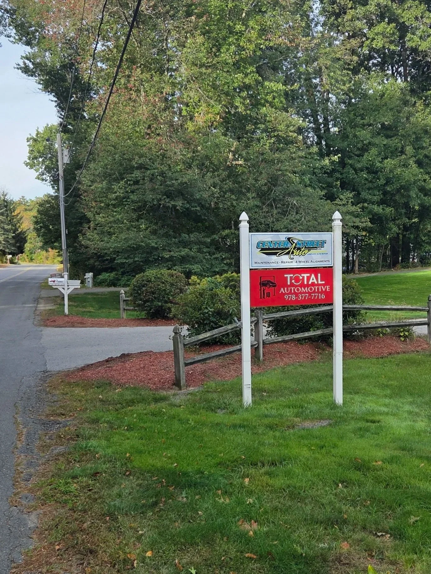 Signboard in front of a dense green forest area with a road on the side, advertising for Center Street Auto and Total Automotive car services.