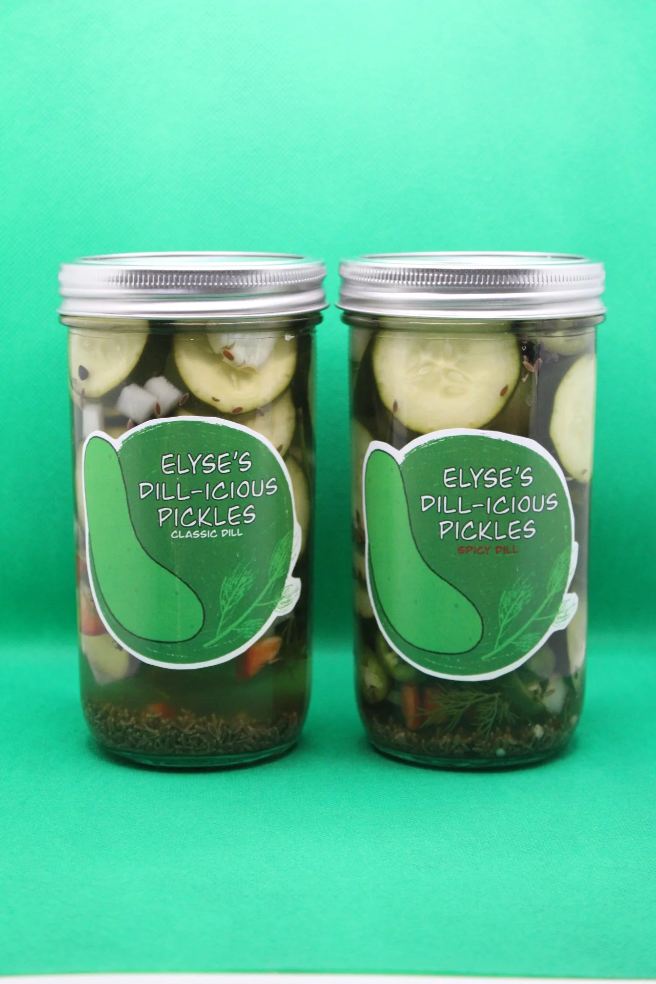 Two jars of Elyse's Dill-icious Pickles, one labeled 'Classic Dill' and the other 'Spicy Dill,' against a green background.