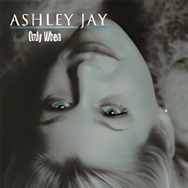 Upside-down close-up of a young woman's face with light-colored hair and blue eyes, with text 'ASHLEY JAY' and partially visible text that might read 'by me' or similar.