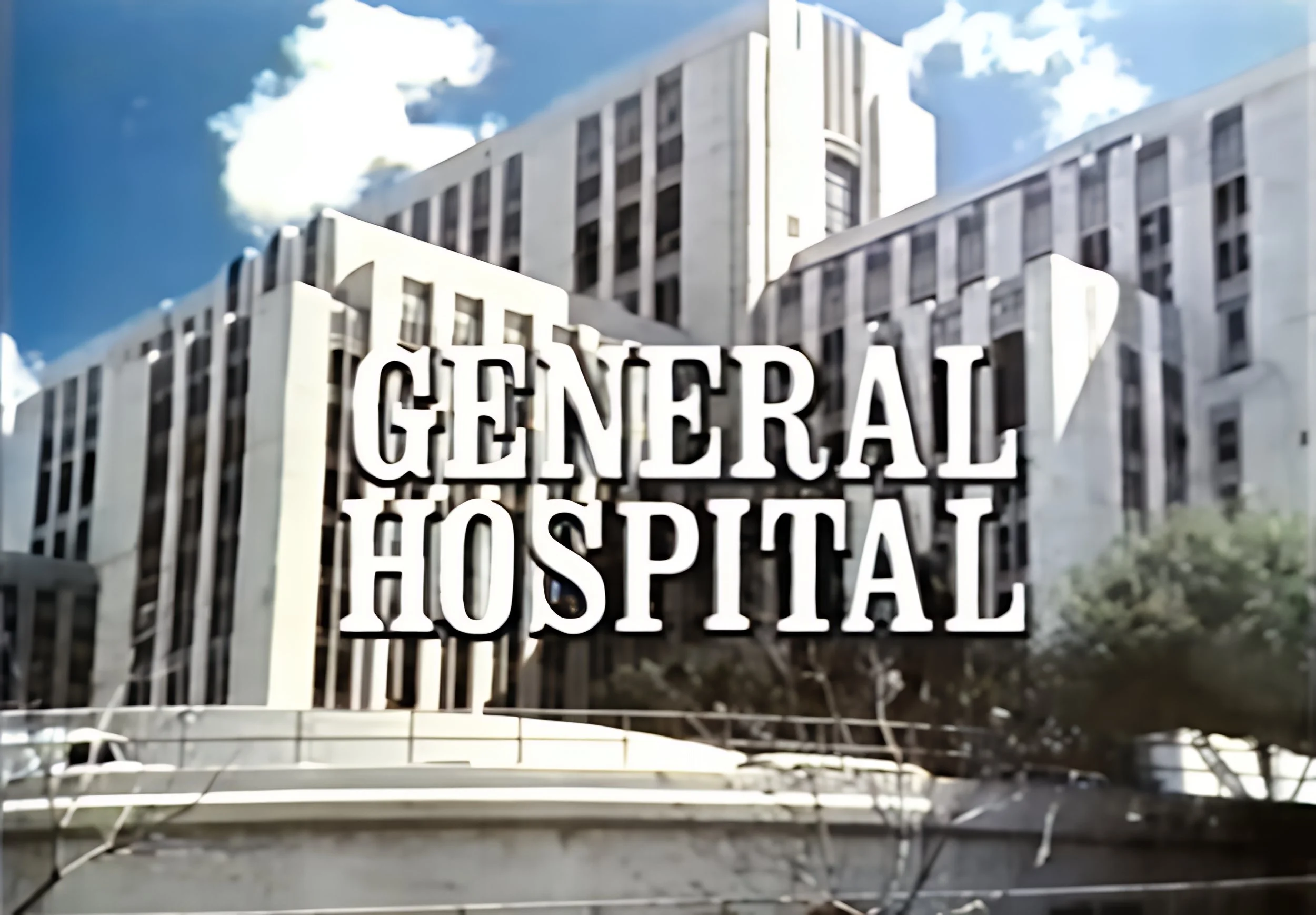 View of a hospital building with a large sign that reads 'GENERAL HOSPITAL' in front and a blue sky with scattered clouds overhead.