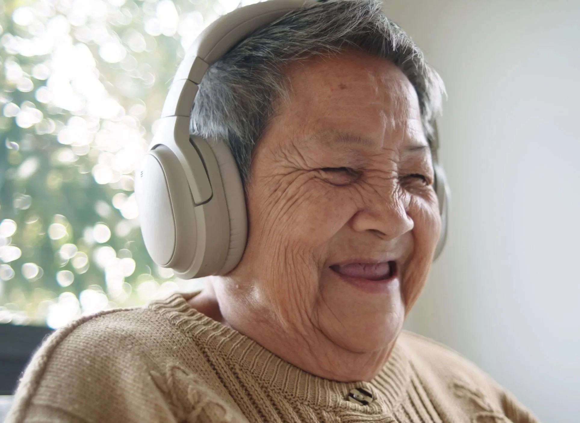 Older woman with short, gray hair wearing large over-ear headphones, smiling with her eyes closed.