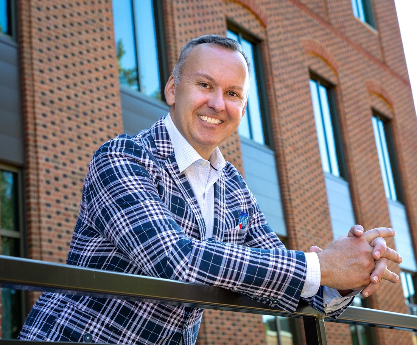 Photo of Jesse in a checkered blue blazer leaning on an office entry rail.