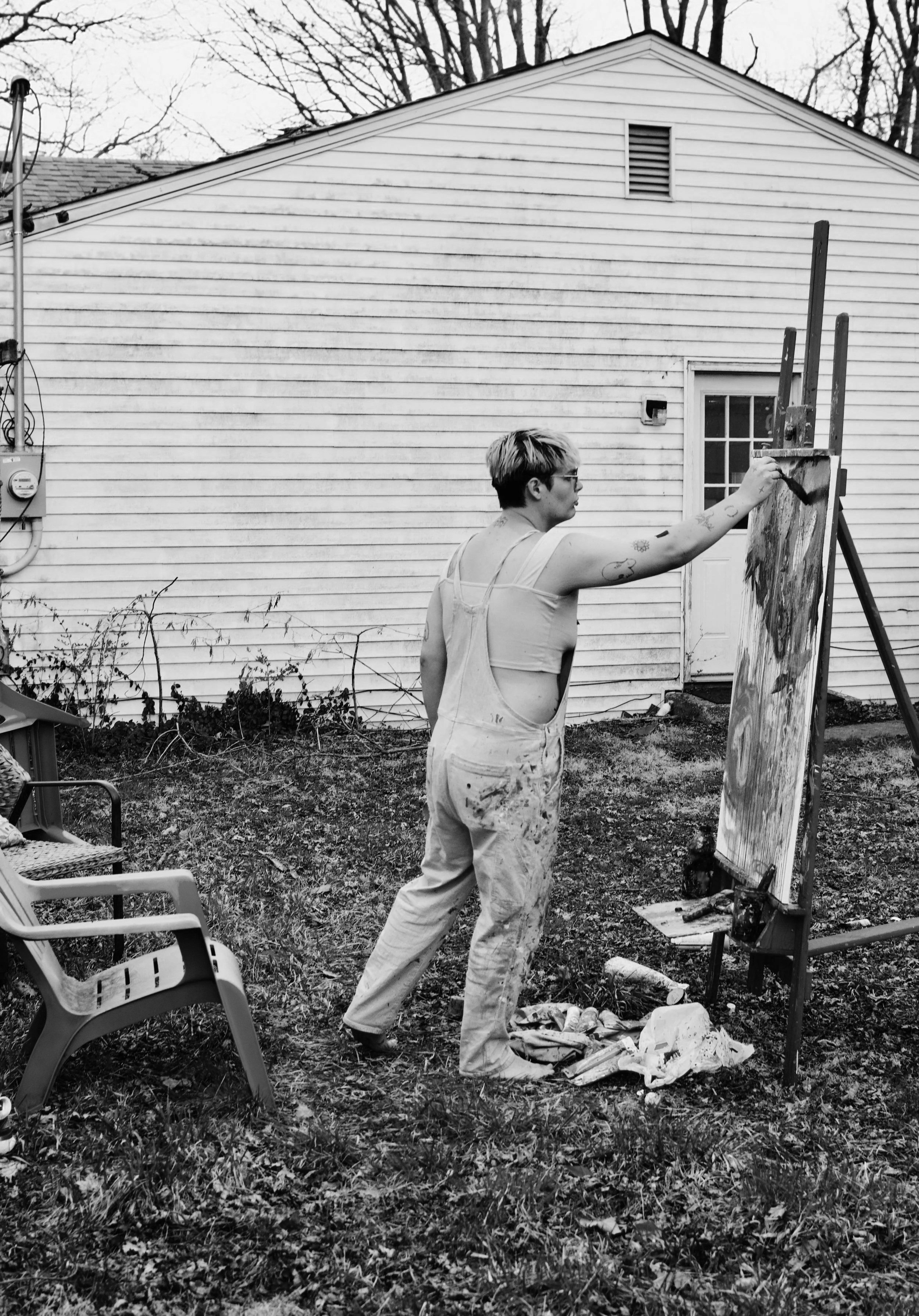 artist Maude Atlas wearing paint-stained overalls, outside painting on a large canvas