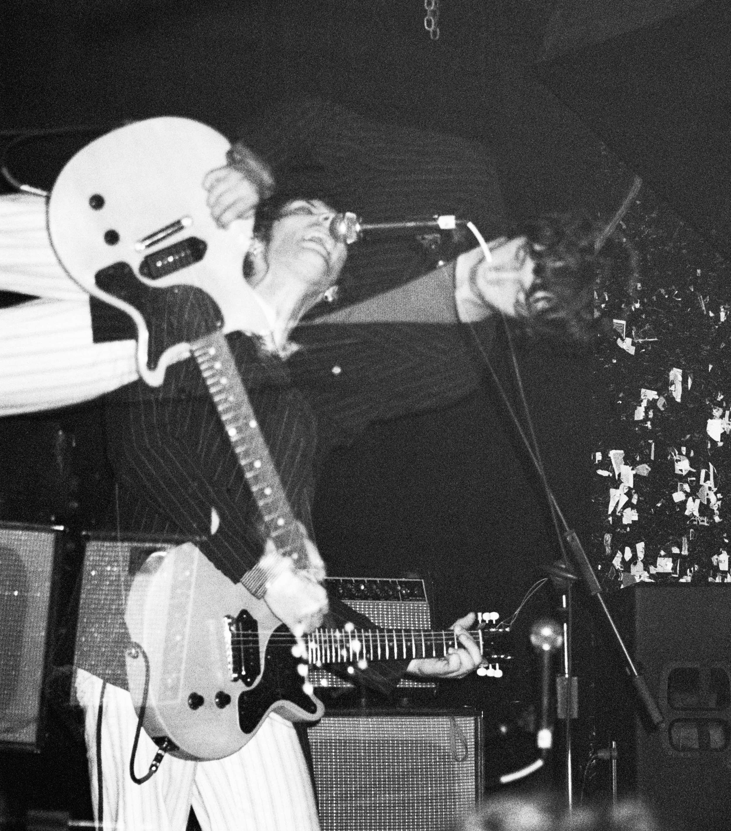 Black-and-white concert photo of a musician in a helmet playing electric guitar and singing into a microphone.