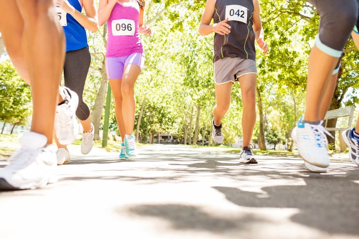 Group of runners participating in a race, running on a tree-lined path on a sunny day.