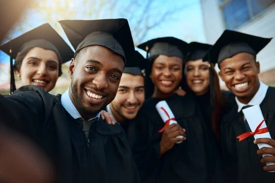 Group of diverse graduates wearing caps and gowns celebrating outdoors.