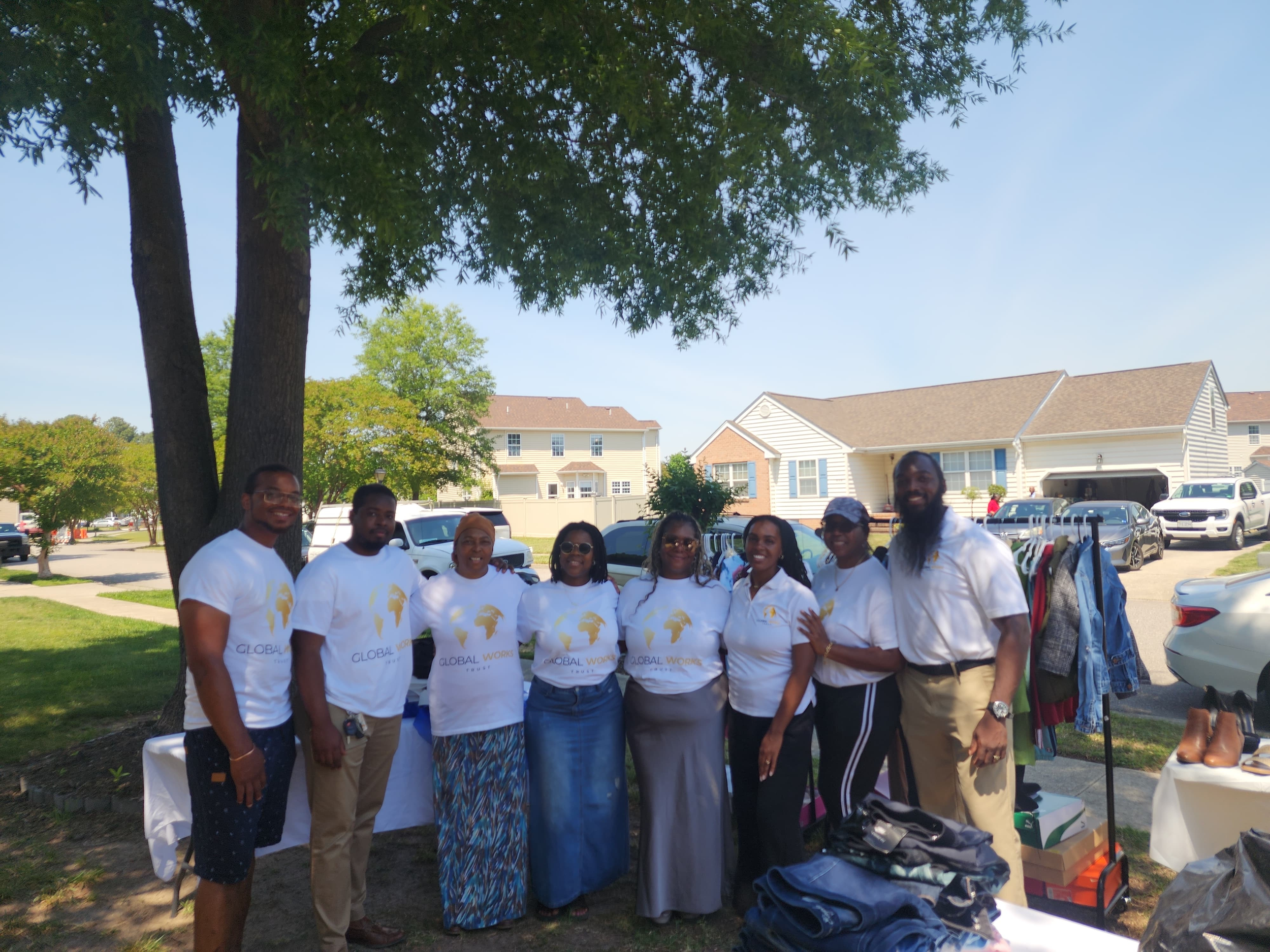 Group of people standing in a park on a sunny day, posing for a photo. They are wearing white shirts with a logo and the words 'Global Works'.