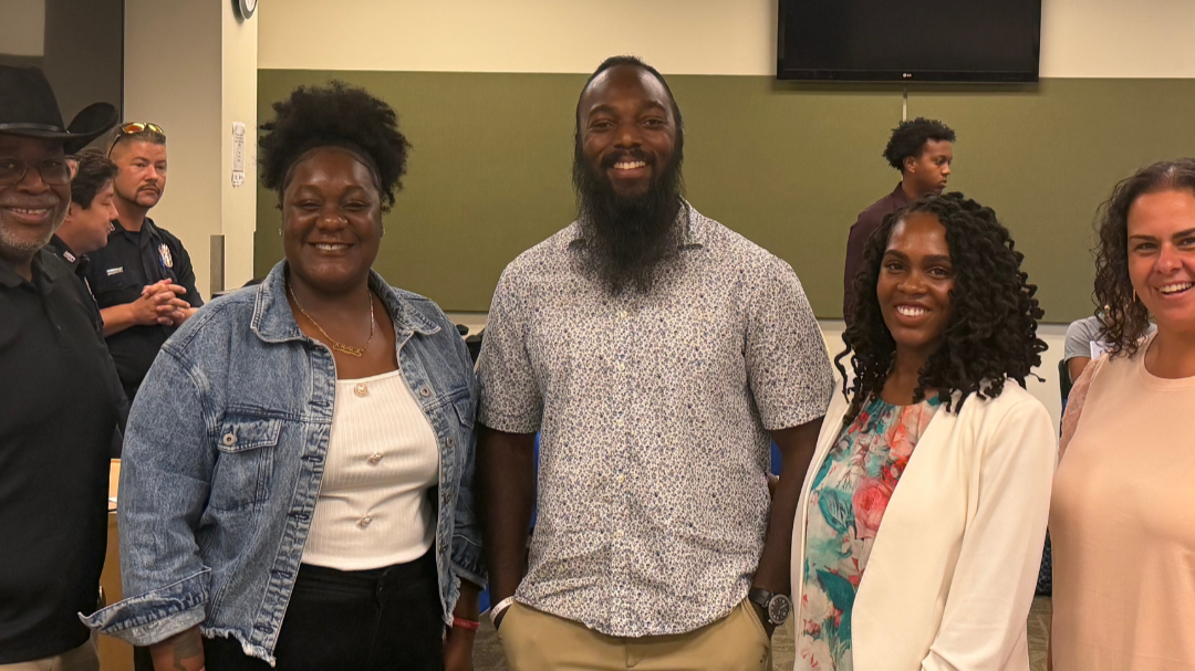 Group of five diverse people smiling and posing indoors at a social or community event.