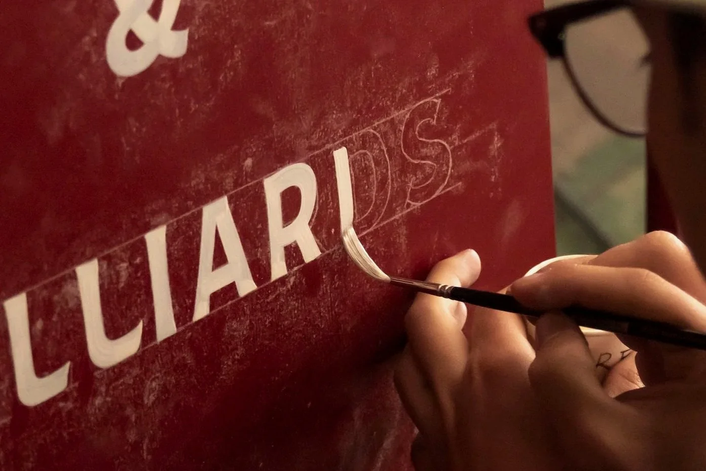 L'artisan Icimarin peignant une enseigne à la main avec des gestes de précision, il réalise une enseigne sur mesure et accompagne le client dans sa conception. Lettrage fait main, conception artisanale.
