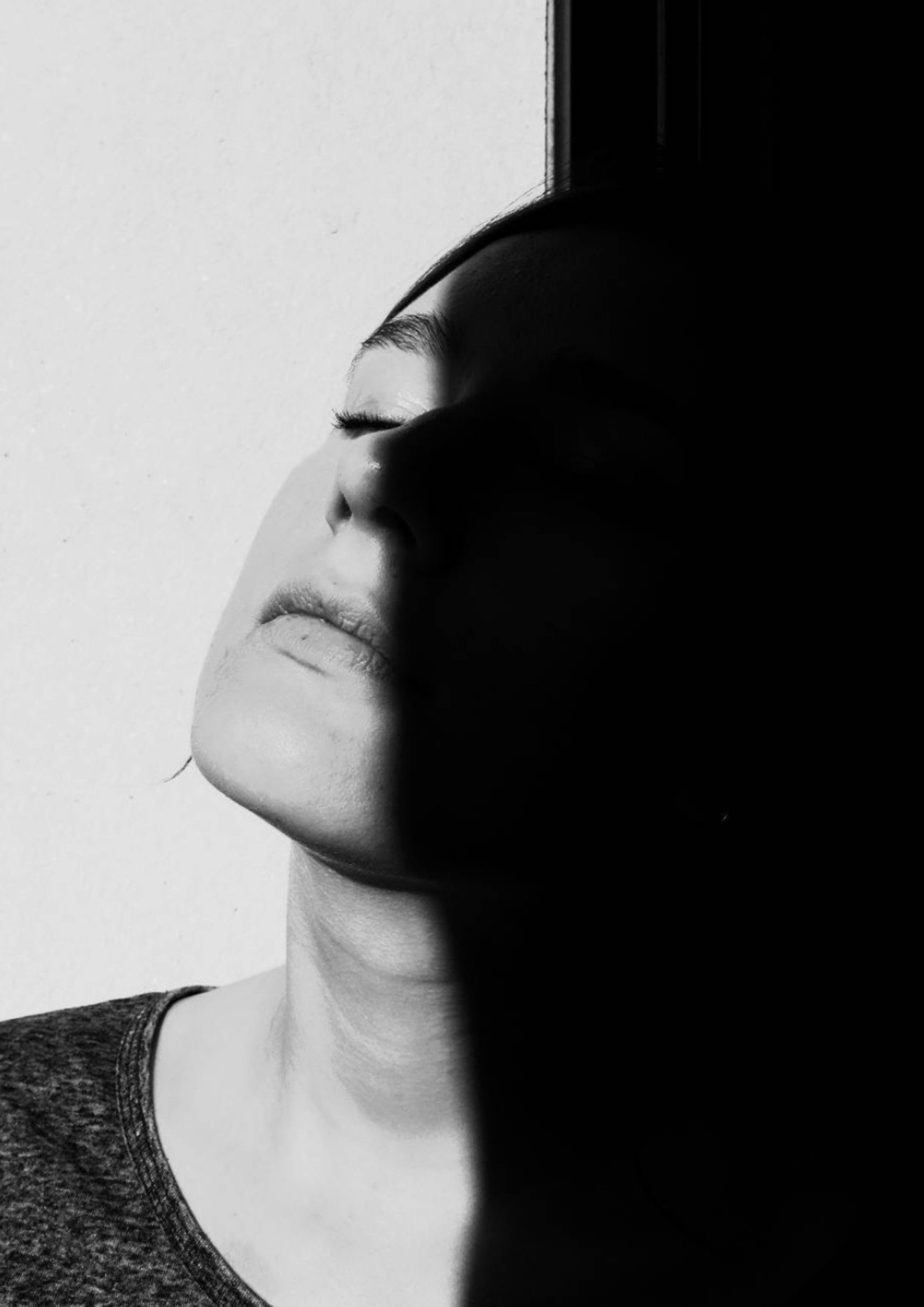 Portrait en noir et blanc d'une femme avec un visage partiellement dans l'ombre, yeux fermés, expression sereine.