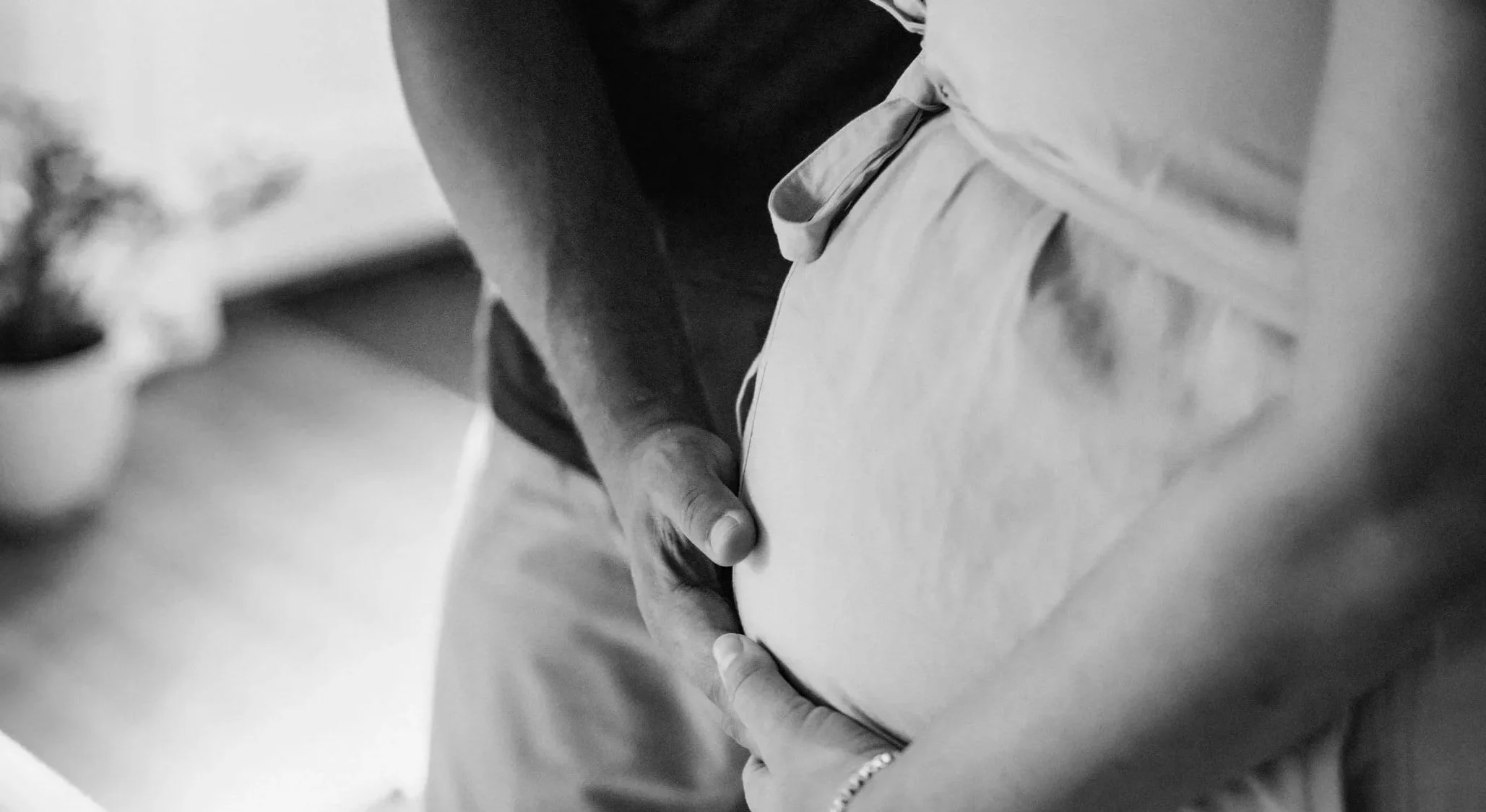 Deux mains sur le ventre d'une femme enceinte, la main d'un homme et celle de la femme. Photo en noir et blanc
