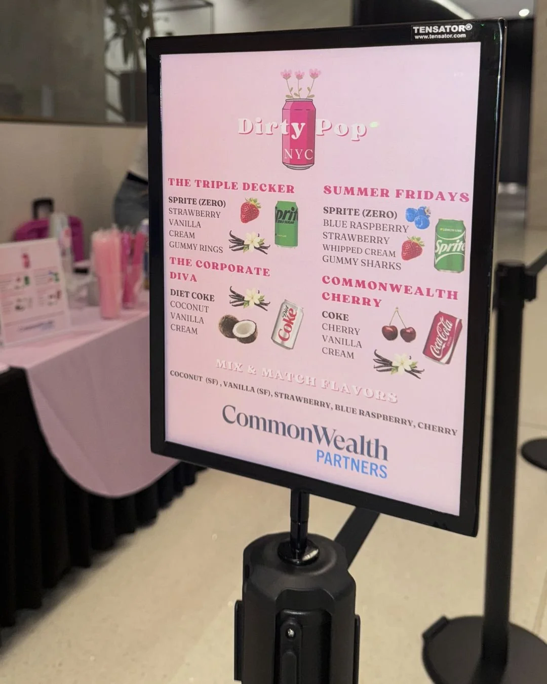 Event menu board with pink background listing various flavored sodas, including 'The Triple Decker' with Sprite zero, strawberry, vanilla, cream, and gummy rings; 'Summer Fridays' with Sprite zero, blue raspberry, strawberry, whipped cream, and gummy sharks; 'The Corporate Diva' with Diet Coke, coconut, vanilla, and cream; and 'Commonwealth Cherry' with Coke, cherry, vanilla, and cream. It also mentions mix and match flavors, and displays logos for Dirty Pop NYC and Commonwealth Partners.