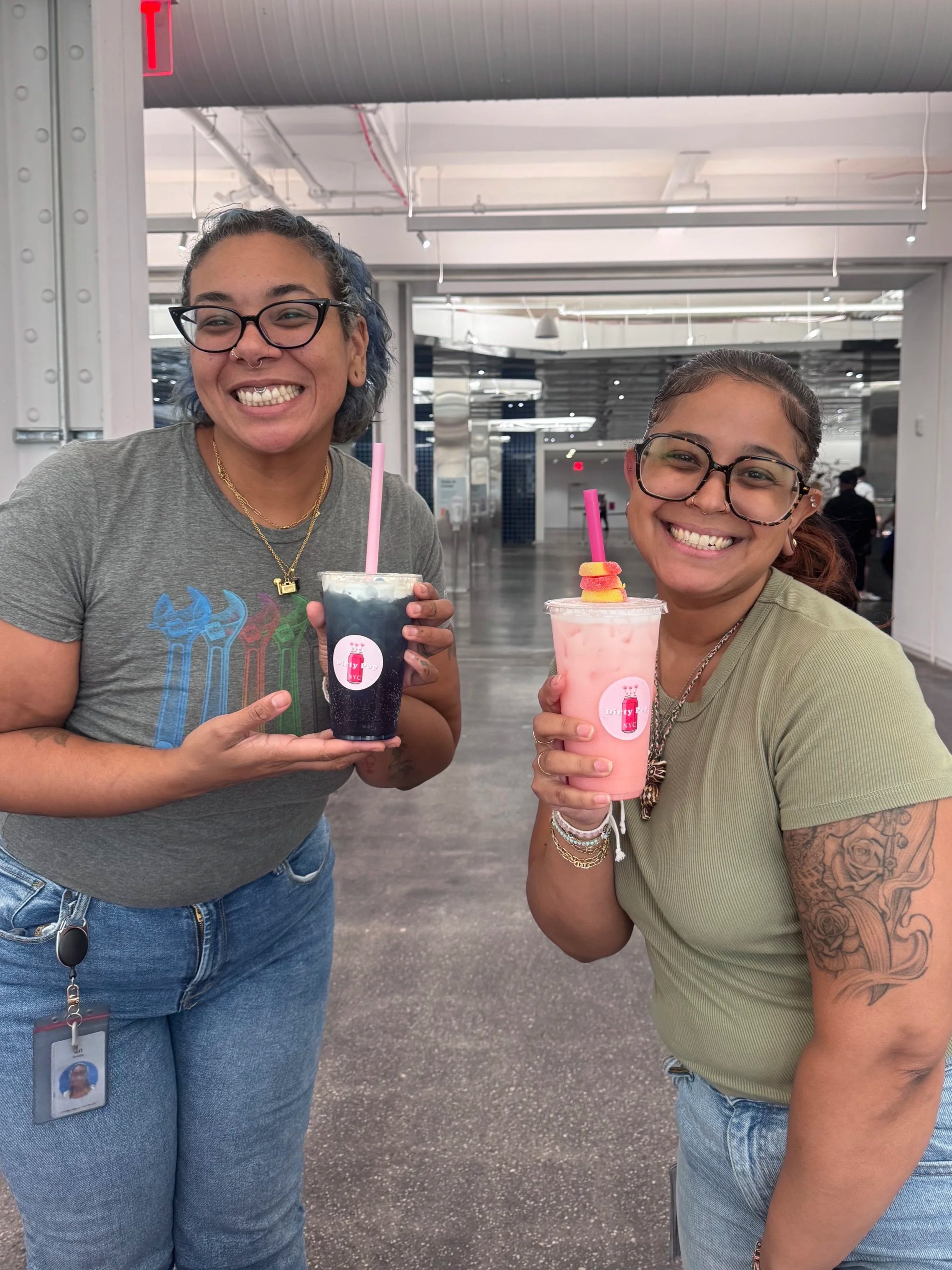 Two smiling women holding bubble tea drinks in an indoor public space.
