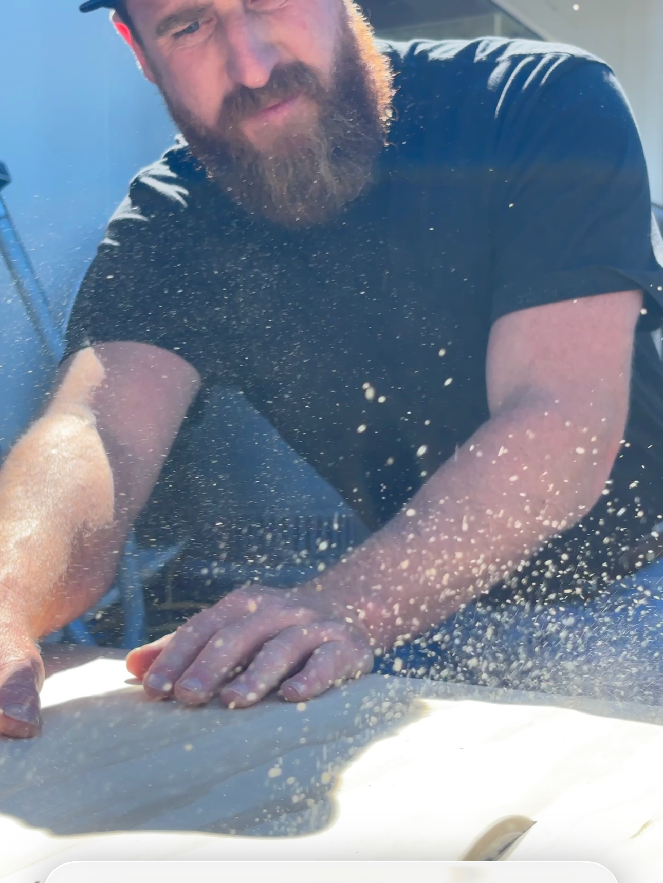 A man with a beard in a black shirt is pressing down with his hands on a flat surface, with dust or powder particles flying up around him.