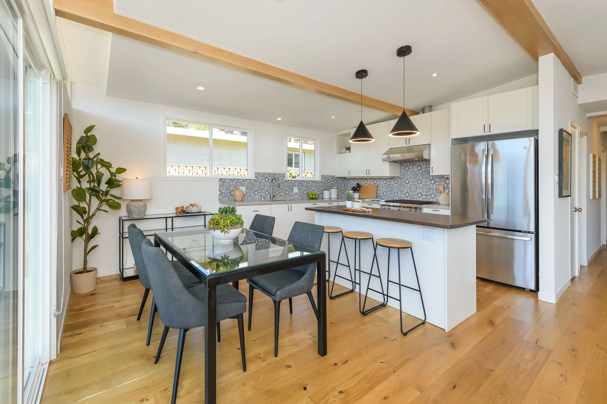 Modern kitchen with white cabinets, patterned backsplash, stainless steel refrigerator, and dining area with glass-top table and black chairs.