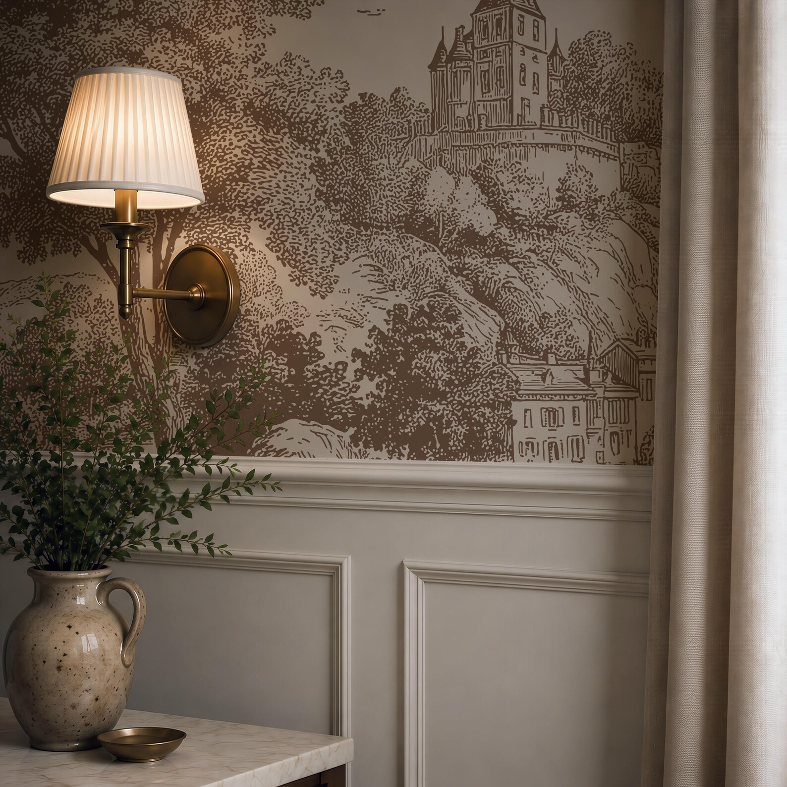 A wall with a vintage illustration of a castle and trees, with a brass wall sconce and a pleated lampshade attached. In the foreground, a ceramic vase with green plant leaves on a marble table.