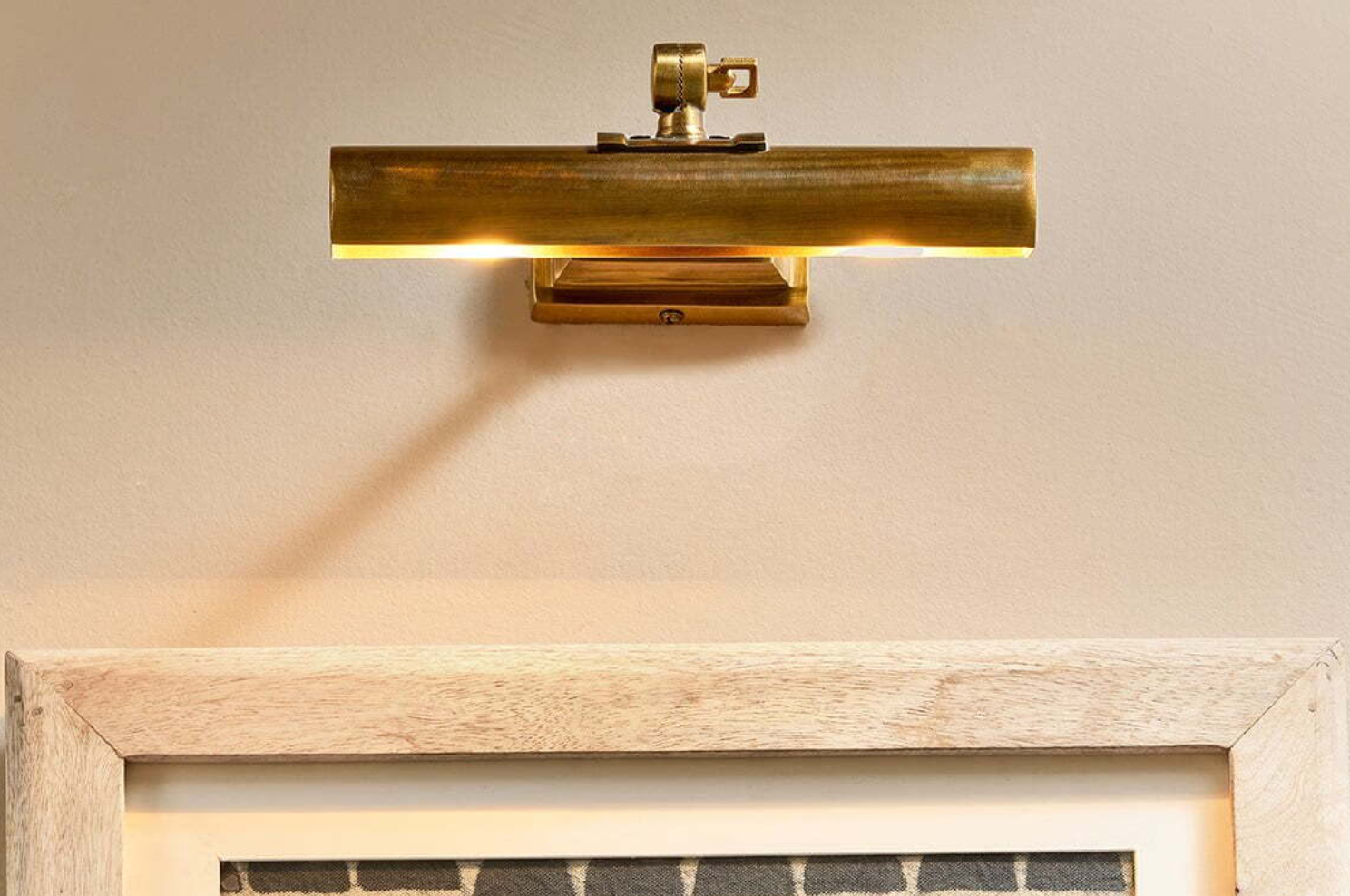 Beautiful brass picture light attached above a wooden frame wall art, illuminating the artwork below.